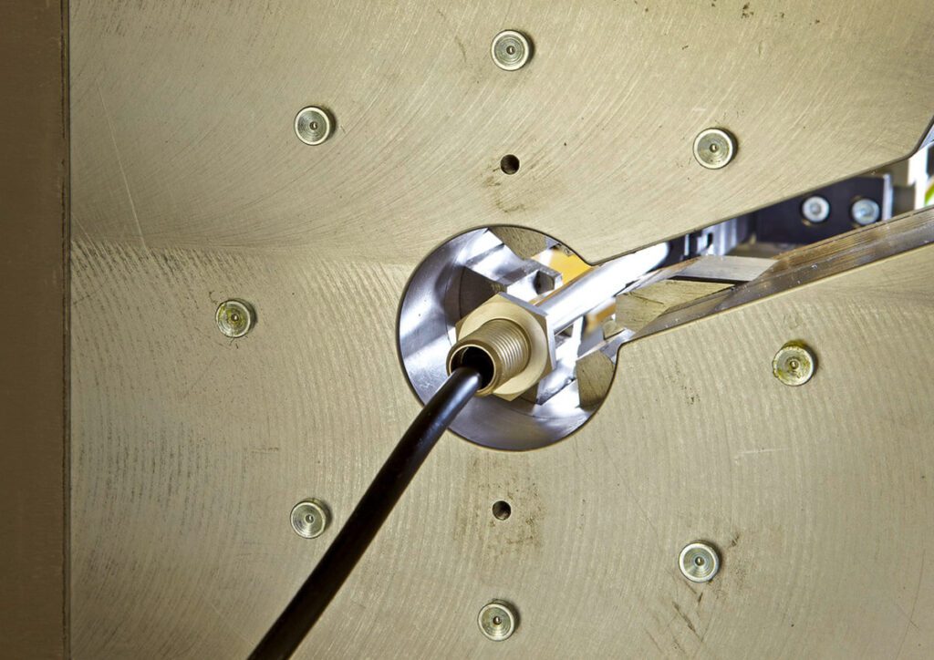 Nahaufnahme einer Maschine beim Bearbeiten eines Metallrohrs mit eingespanntem Kabel im Werkzeugkopf