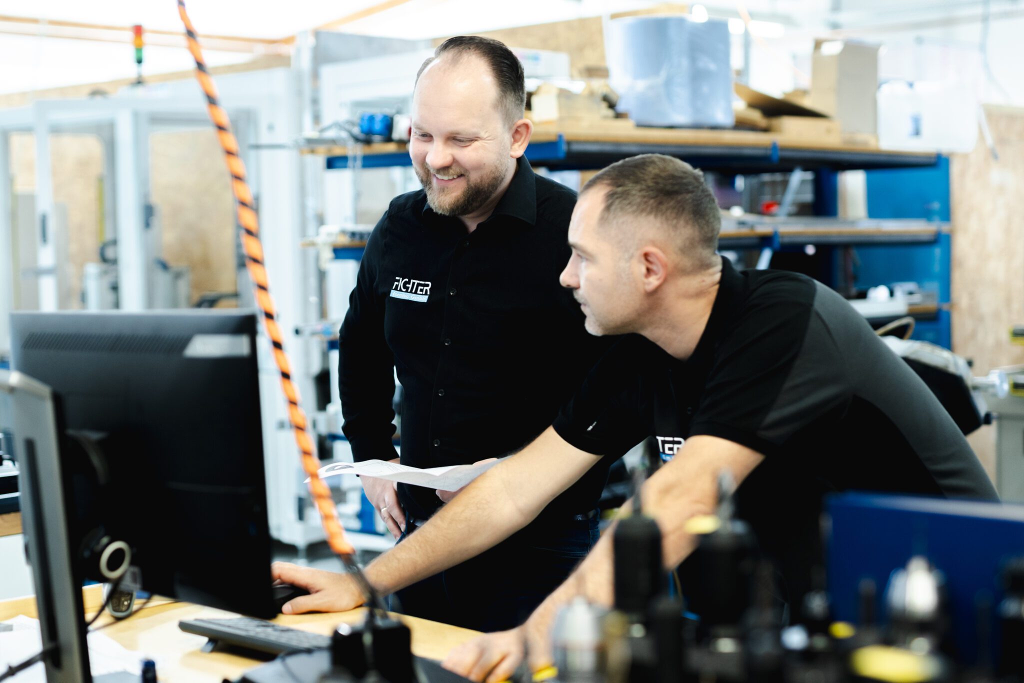 Zwei Mitarbeiter in der Fertigungshalle im Gespräch – Zusammenarbeit und Abstimmung an der Maschine