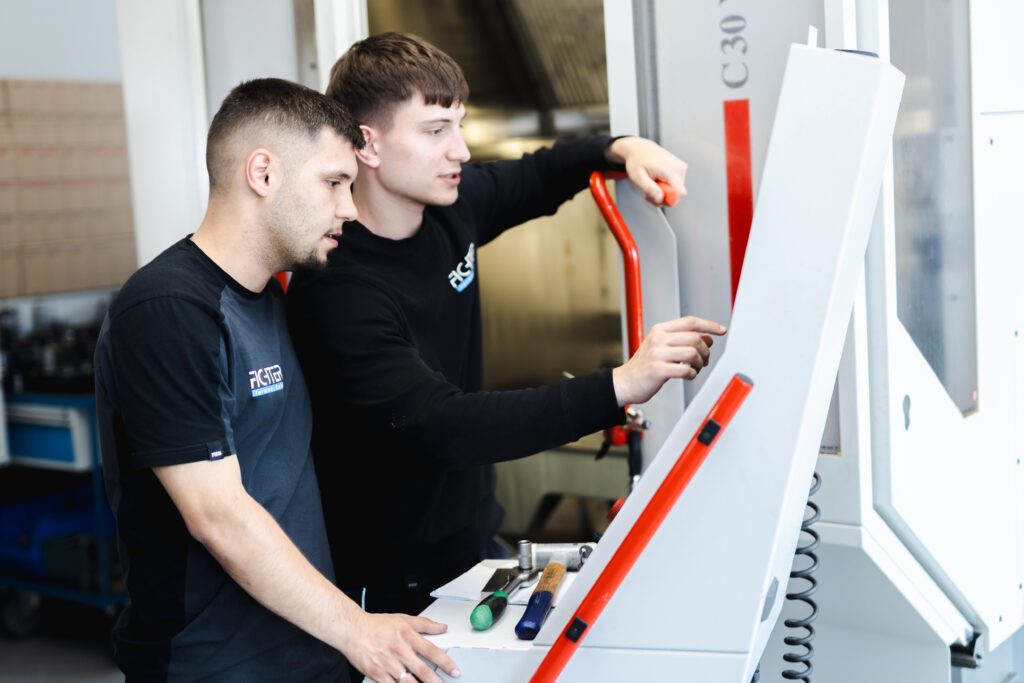 Zwei Mitarbeiter bedienen gemeinsam eine CNC-Maschine über das Steuerpult in der Fertigungshalle