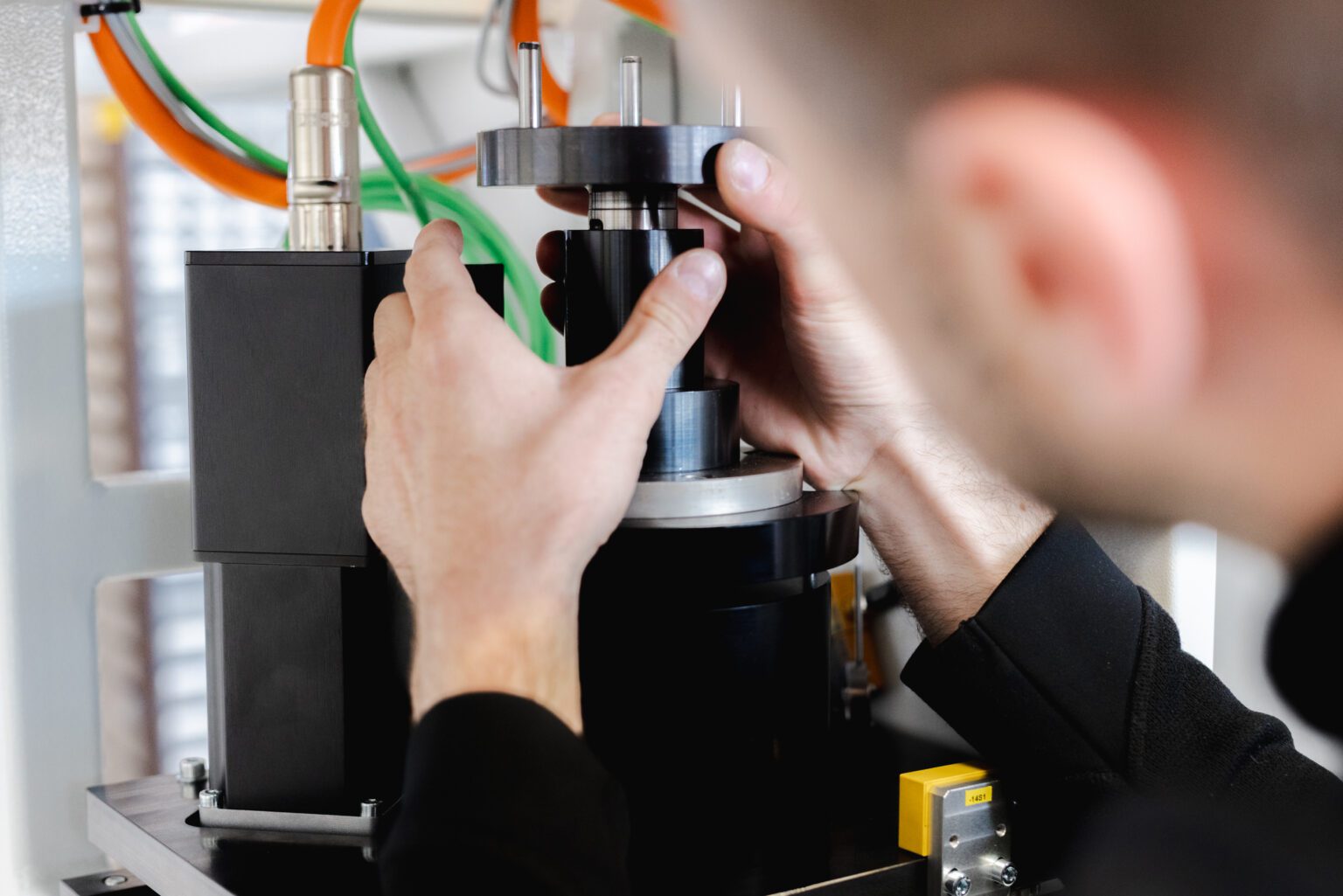 Mitarbeiter montiert ein Bauteil an einer industriellen Maschine mit Kabel- und Schlauchverbindungen im Hintergrund