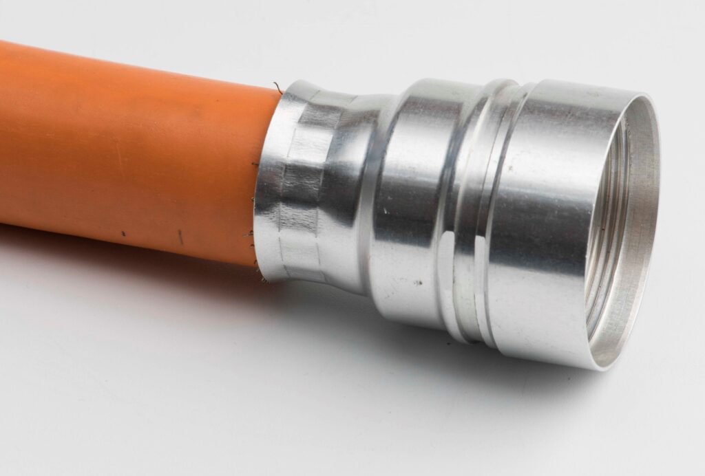 Nahaufnahme eines orangefarbenen Kabels mit aufgebrachtem silbernem Metallanschlussstück in zylindrischer Form