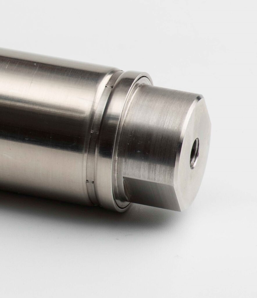 Detailaufnahme eines zylindrischen, aus Edelstahl gefertigten Maschinenteils mit glatter Oberfläche und präzise gefräster Stirnseite