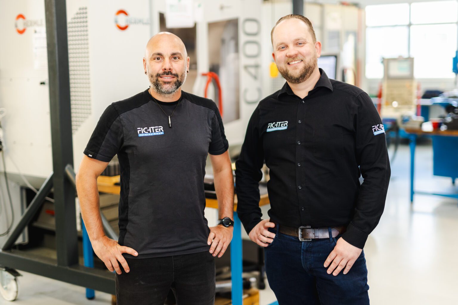 Geschäftsführer von Fichter formtec stehen in der Werkstatt und lächeln in die Kamera