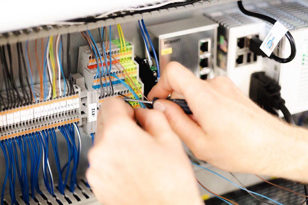 Nahaufnahme von Händen, die Kabel in einem Schaltschrank anschließen und elektrische Verbindungen herstellen